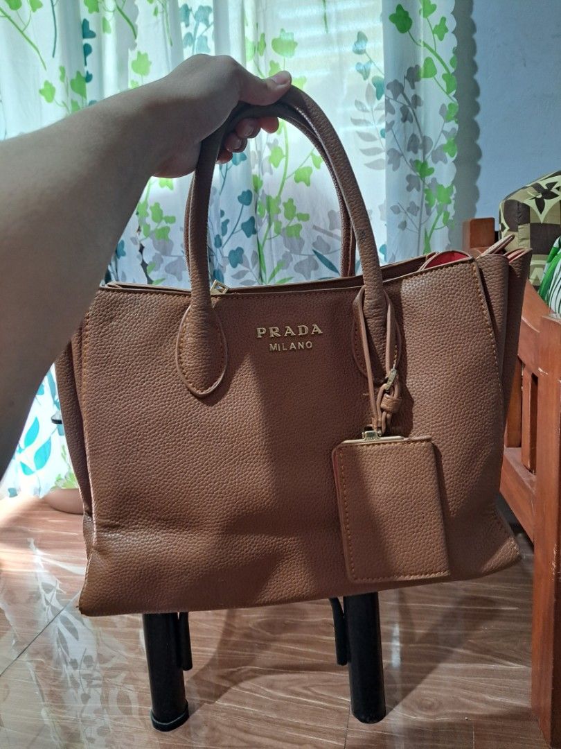 Prada Milano Brown Bag (Category: Luxury Bags & Wallets) located in Mandaluyong City. Submitted by teeniethriftee (Listing ID 1419450657, Image 2). Description: - Brown Prada Milano tote bag - Top handle design - Includes a small attached pouch - Red interior lining - Features a zippered compartment - Gold Prada Milano logo - Made of leather - bought from canada. - with sign of usages but can be repaired by the buyer..