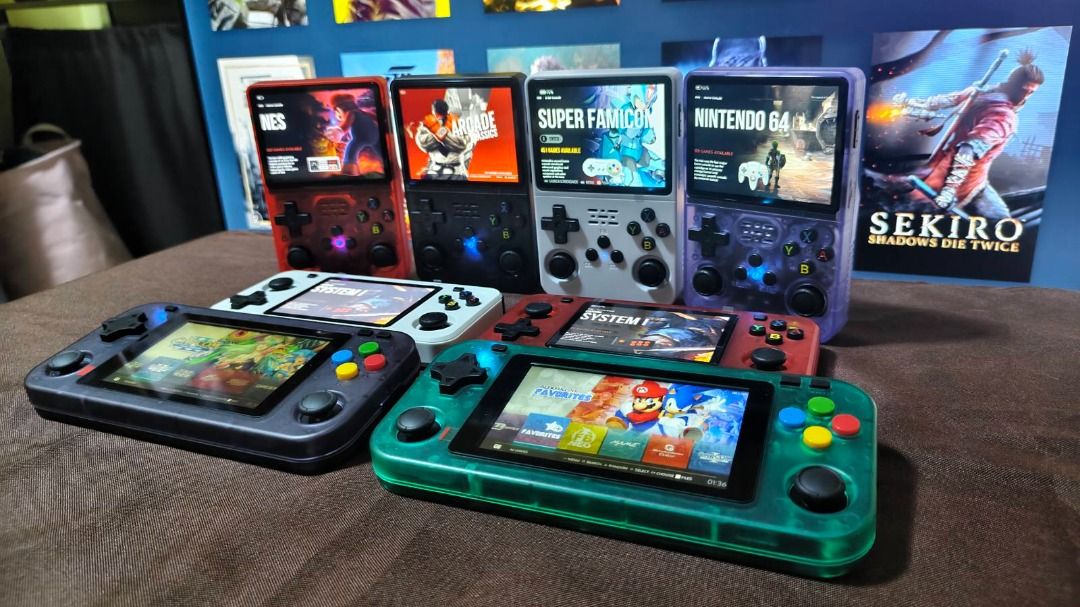 Retro Handheld Game Console (Category: Others) located in Davao. Submitted by leovanniem23152 (Listing ID 1419398131, Image 2). Description: Collection of retro handheld game consoles in various colors. Each console features a screen displaying different game interfaces. The consoles have a D-pad, buttons, and analog sticks. Some consoles show NES, Super Famicom, and Nintendo 64 game interfaces. The consoles come in red, black, white, gray, and g
