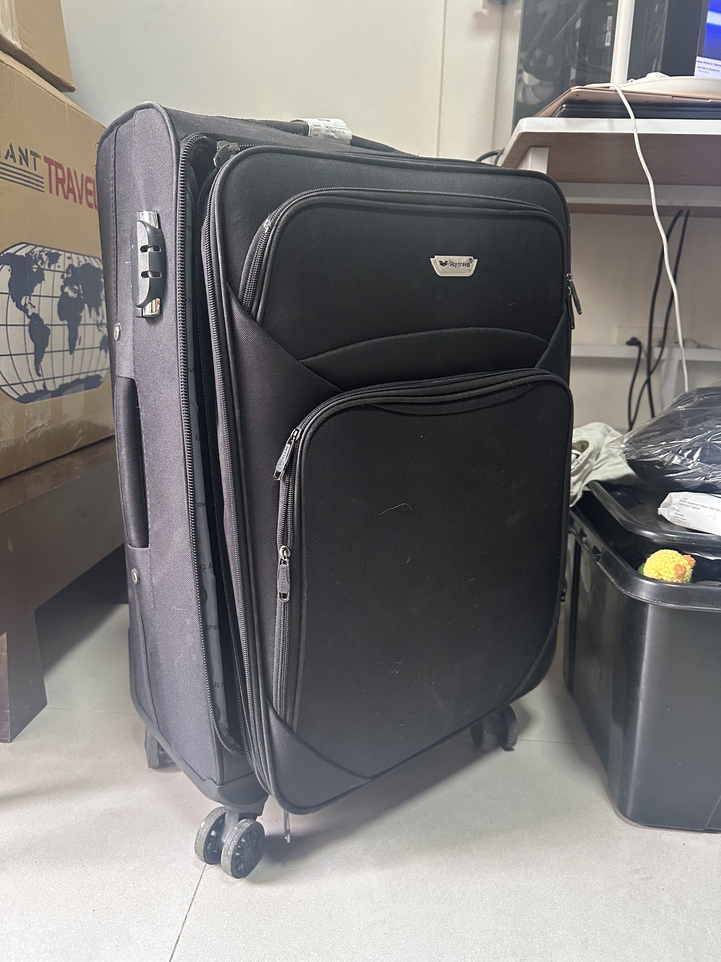 Sky Travel Black Rolling Luggage (Category: Luggage) located in Taguig. Submitted by ylluhhhh (Listing ID 1419570976, Image 2). Description: Black rolling luggage with multiple compartments. Features a combination lock for security. The interior is lined with a Sky Travel branded fabric. Includes wheels for easy transport. Zippers are visible on the front pockets. Size: M .