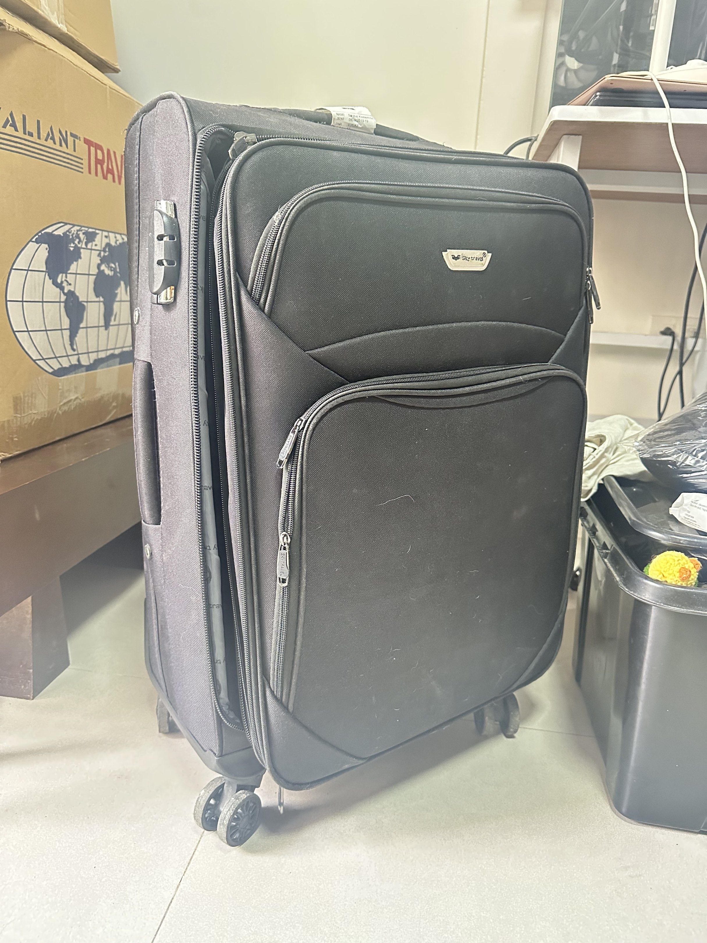 Sky Travel Black Rolling Luggage (Category: Luggage) located in Taguig. Submitted by ylluhhhh (Listing ID 1419570976, Image 1). Description: Black rolling luggage with multiple compartments. Features a combination lock for security. The interior is lined with a Sky Travel branded fabric. Includes wheels for easy transport. Zippers are visible on the front pockets. Size: M .