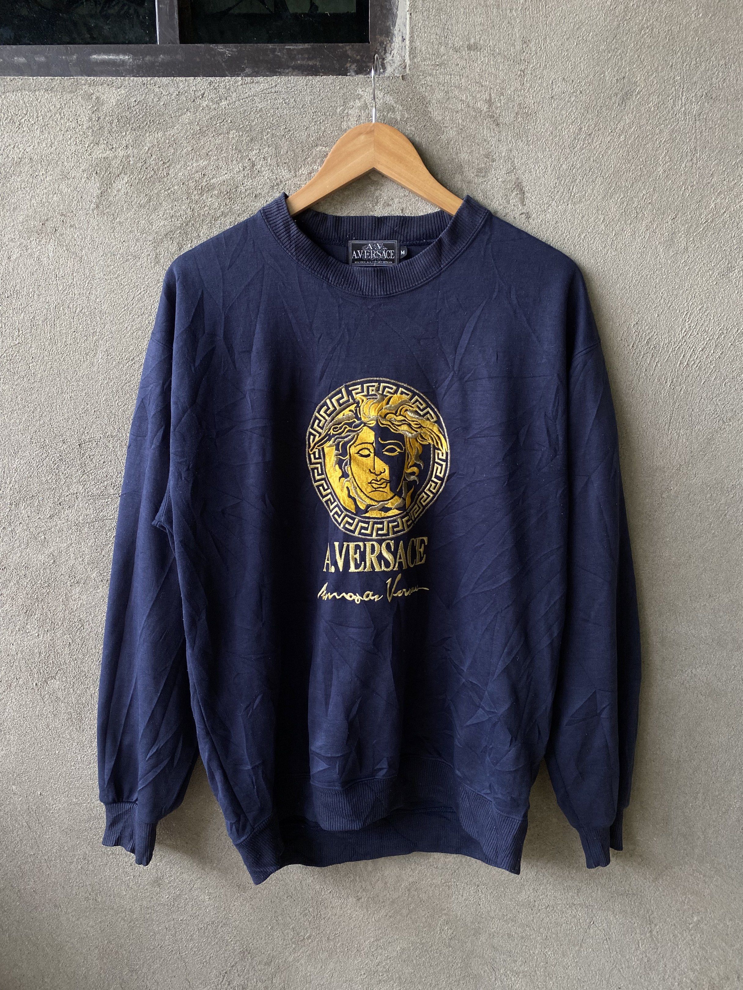 A. Versace Medusa Sweatshirt - Navy Blue (Category: Coats, Jackets and Outerwear) located in Tuguegarao City. Submitted by thriftnigelo (Listing ID 1419595389, Image 1). Description: Navy blue A. Versace sweatshirt featuring a gold Medusa head logo on the front. The label indicates it's from A.V. Versace Diffusion line. It has a crew neck and long sleeves. The size is medium. The sweatshirt has a vintage look..
