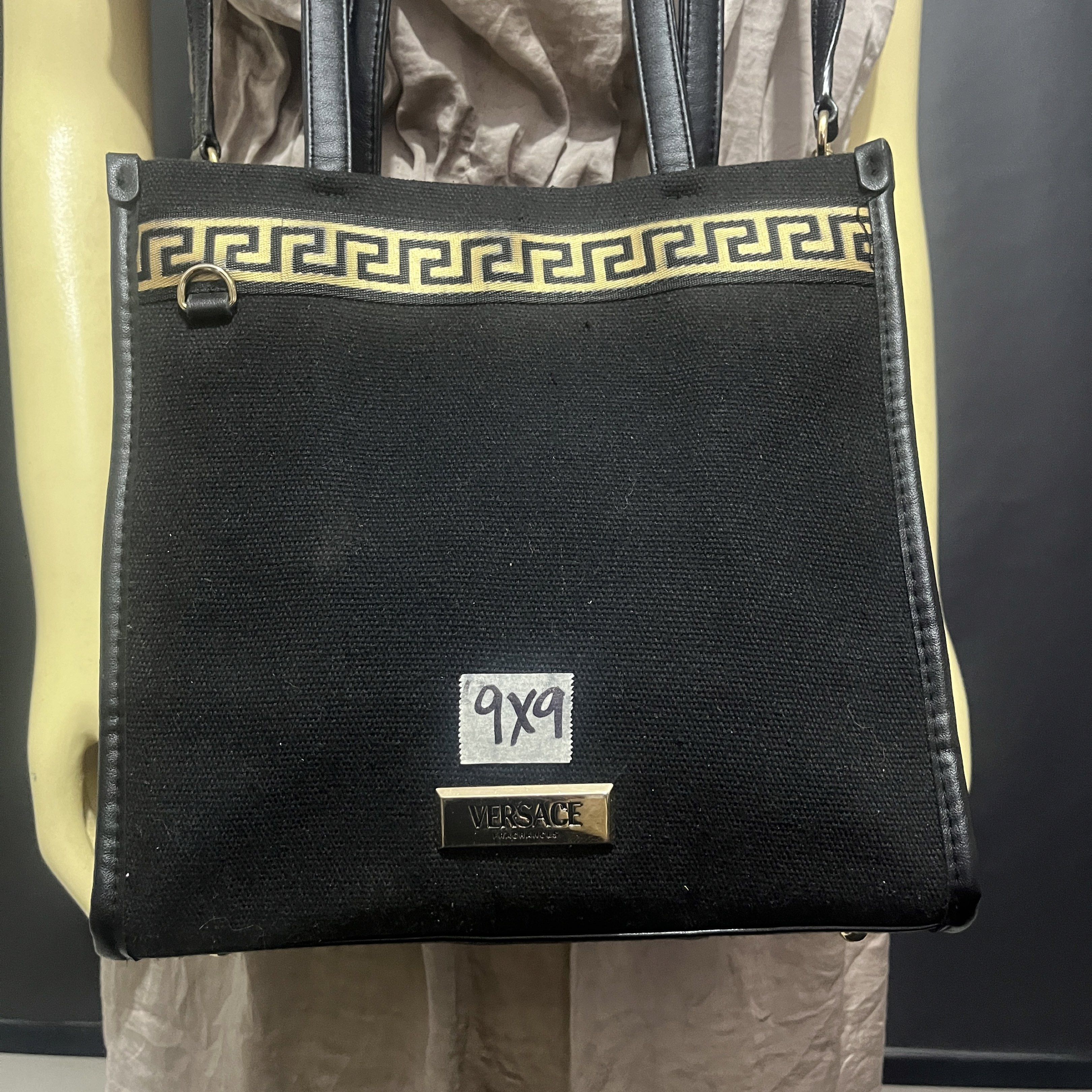 Versace Black Tote Bag with Shoulder Strap (Category: Luxury Bags & Wallets) located in Butuan. Submitted by dfgthriftology2.0 (Listing ID 1419721066, Image 2). Description: - Versace tote bag - Black canvas and leather exterior - Gold Greek key design - Detachable shoulder strap - Top handles - Rectangular shape - Black interior lining - Versace logo on front - Small interior pocket.