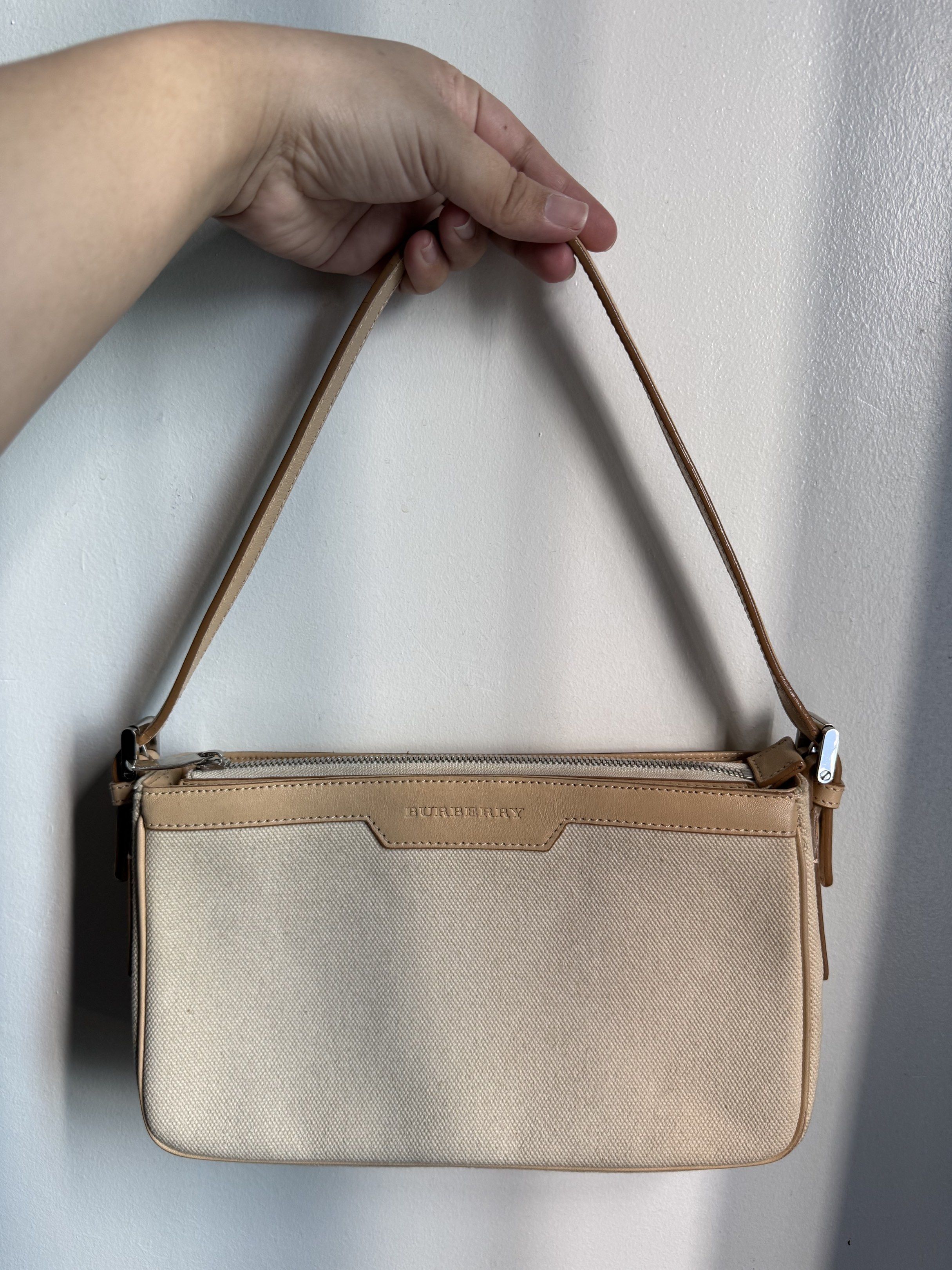 Burberry canvas baguette (Category: Luxury Bags & Wallets) located in Malolos. Submitted by prelovedbydrjen (Listing ID 1419820496, Image 1). Description: - Authentic Burberry shoulder bag - Beige canvas exterior with leather trim - Secure top zipper closure - Comfortable single shoulder strap - Classic Burberry check interior lining - Includes an additional pocket - Compact and ideal for daily wear.