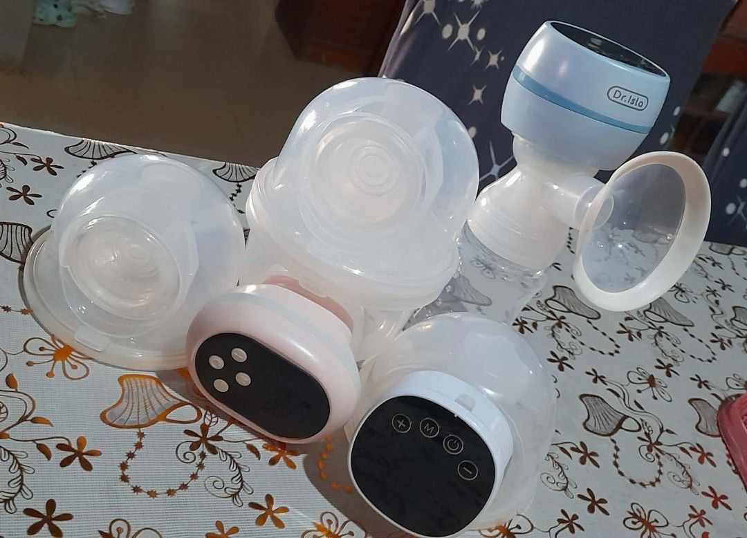 Dr. Isla Electric Breast Pump (Category: Breastfeeding & Bottle Feeding) located in San Fernando. Submitted by masterambrose13 (Listing ID 1419795604, Image 1). Description: - Electric breast pump set - Includes two pump units: - Pink unit - Dr. Isla blue unit - Comes with bottles and other accessories - Features control buttons for easy operation - Items are on a floral patterned surface.