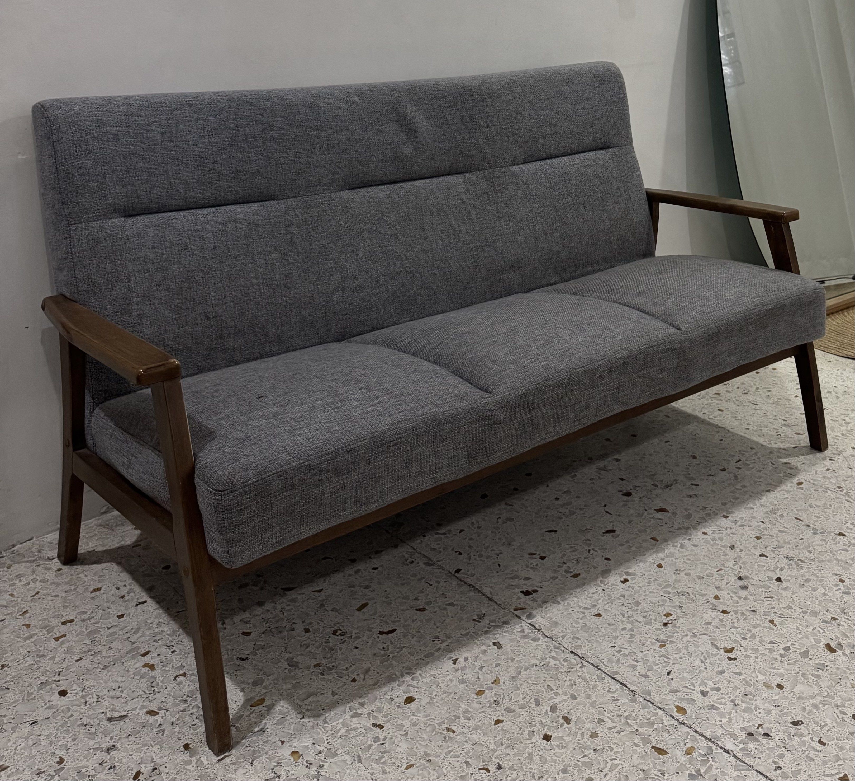 Mid-Century Modern 3-Seater Sofa (Category: Sofas) located in Caloocan City. Submitted by andii.rhei (Listing ID 1419858102, Image 1). Description: - 3-seater sofa - Mid-century modern design - Gray fabric upholstery - Wooden frame and armrests - Clean, minimalist aesthetic - Ideal for living rooms and lounges -Cotton fabric seat - Three-section cushions - Sturdy wooden legs.