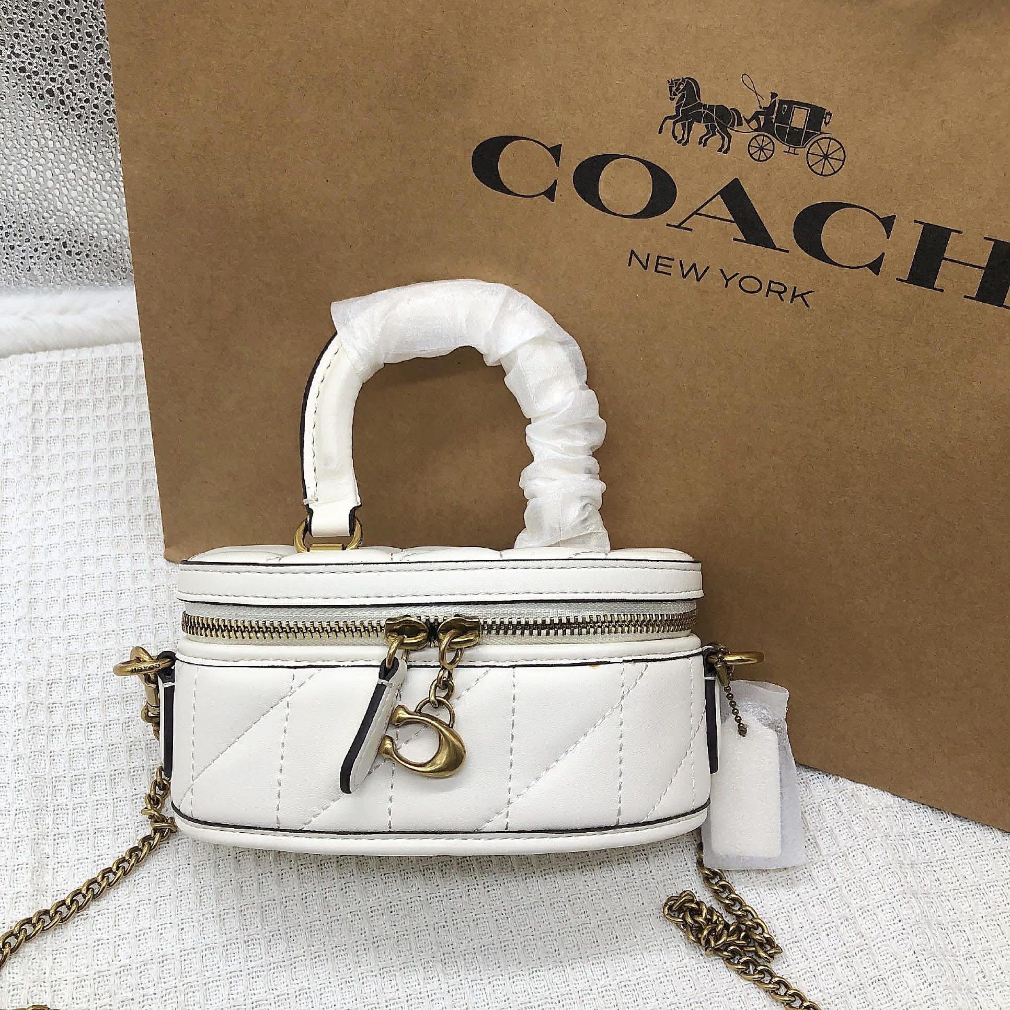 Coach Vanity Case Crossbody Bag (Category: Luxury Bags & Wallets) located in Manila. Submitted by clairetot (Listing ID 1420093993, Image 1). Description: Coach vanity case crossbody bag features a white quilted design. It has a top handle and a chain strap. The bag includes a zipper closure and a Coach charm. It comes with a tag attached. The bag is new and unused..