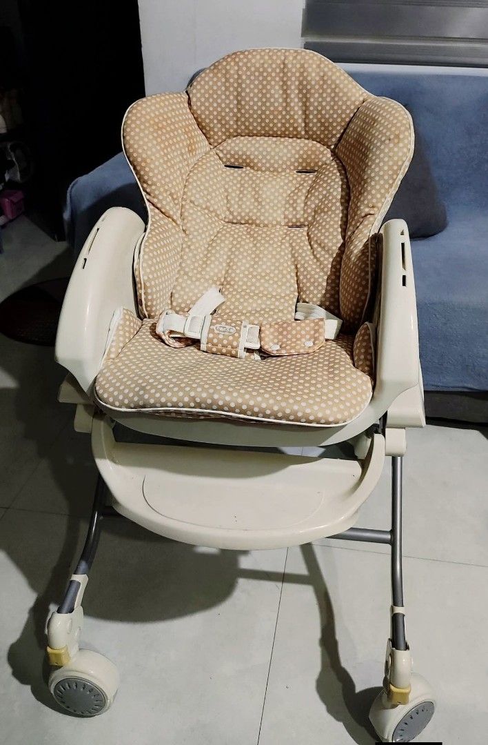 Combi Baby High Chair (Category: Baby High Chairs) located in Manila. Submitted by liraalcala63872 (Listing ID 1420098345, Image 1). Description: Combi baby high chair features a beige polka dot seat and a tray. It has a reclining function and wheels for easy movement. It includes safety straps to secure the baby. The chair's frame is a neutral color, and the seat is padded for comfort. preloved with sign of usage .