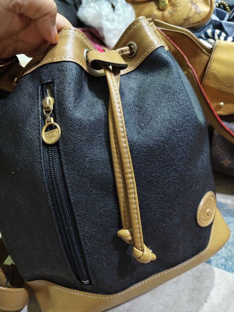 Duck Bucket Bag (Category: Tote Bags) located in Kuala Lumpur. Submitted by luckyshark-ff78f4 (Listing ID 1415873957, Image 2). Description: Stylish Duck bucket bag. Features a drawstring closure and a long shoulder strap. The bag has a two-tone design with a black body and tan accents. The base of the bag is tan, and the strap is also tan. The bag has a pig tapak of 26cm. Perfect for everyday use..