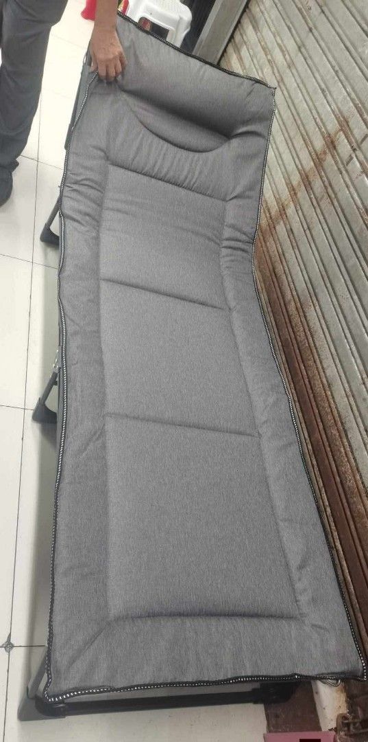 Folding Bed with Gray Cushion (Category: Bed Frames & Mattresses) located in Taguig. Submitted by diannecaya86853 (Listing ID 1420042510, Image 1). Description: - Foldable bed for easy storage - Gray cushioned surface - Black bed frame - Rectangular shape with padded headrest - Stitched detailing and border on the cushion.