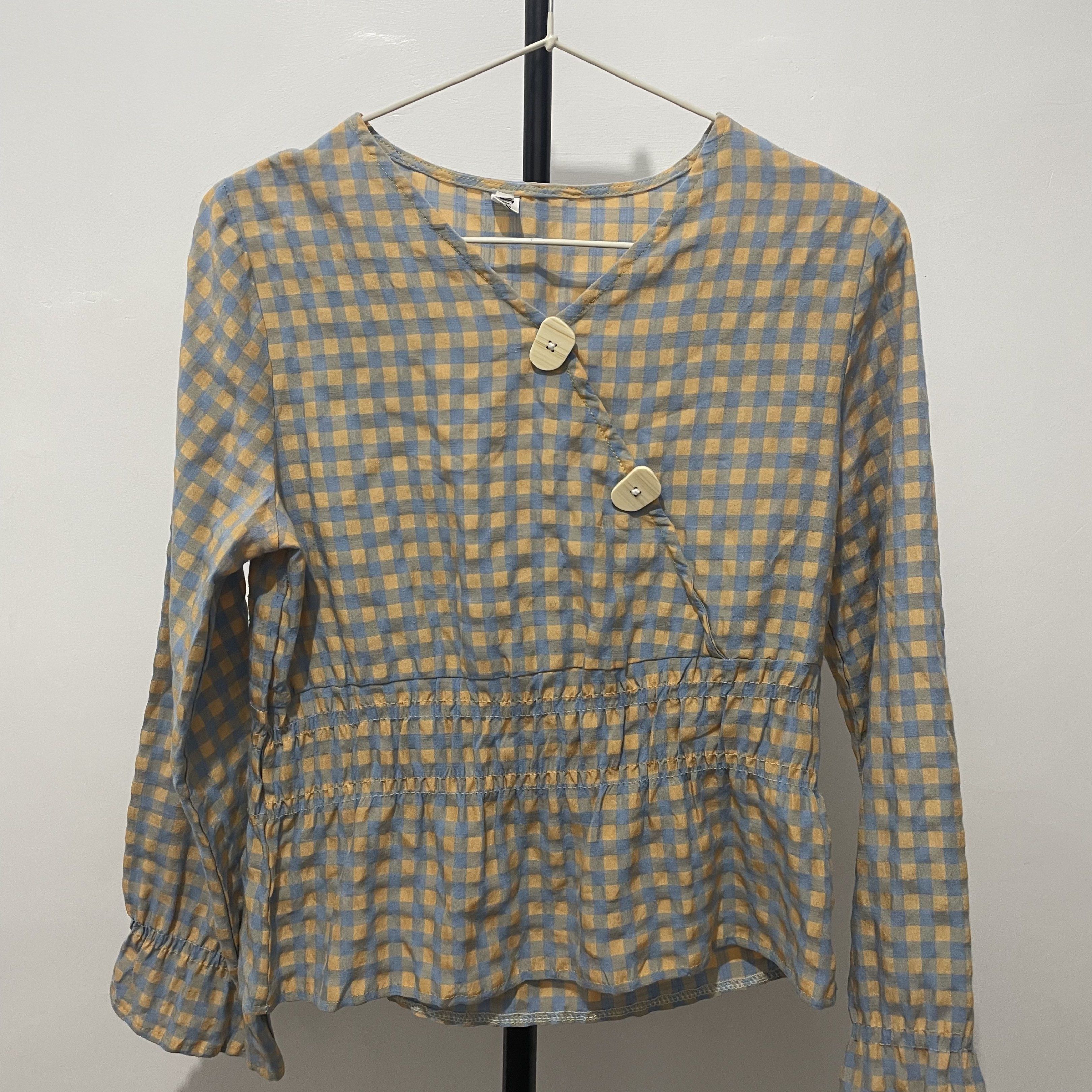 Gingham Check Blouse with Wooden Buttons (Category: Blouses) located in Manila. Submitted by reloom (Listing ID 1420120594, Image 1). Description: - can be for small to medium -Gingham check pattern in blue and yellow - Long sleeves with ruffled cuffs - Cinched waist - V-neckline - Fastened with two wooden buttons - Lightweight fabric.