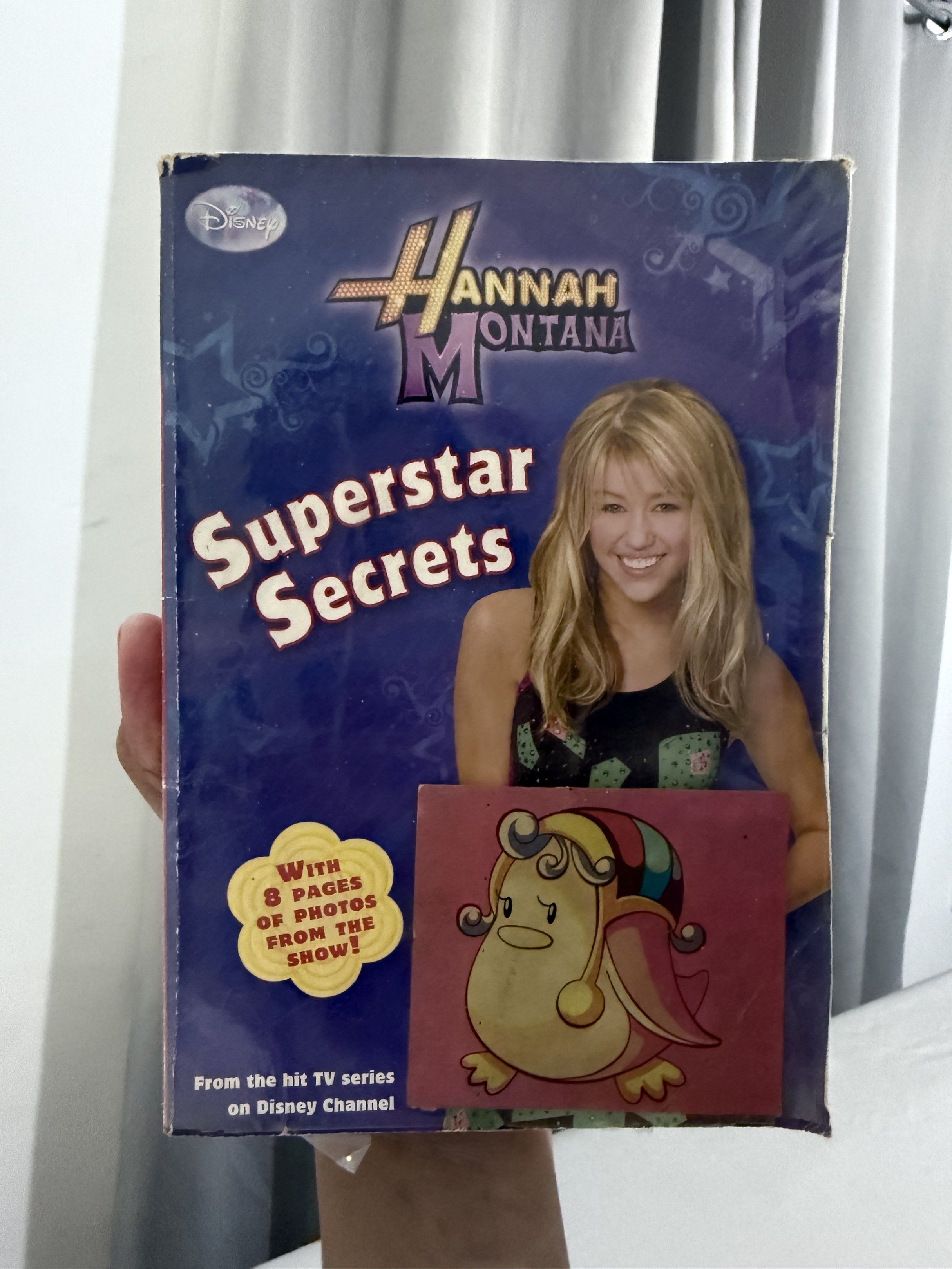 Hannah Montana Superstar Secrets Book (Category: Children's Books) located in Mansalay. Submitted by declutterandco (Listing ID 1420086357, Image 1). Description: - Hannah Montana book from the Disney Channel series. - Includes 'Superstar Secrets'. - Features 8 pages of photos. - Cover features Miley Cyrus as Hannah Montana. - Includes a cartoon character sticker..