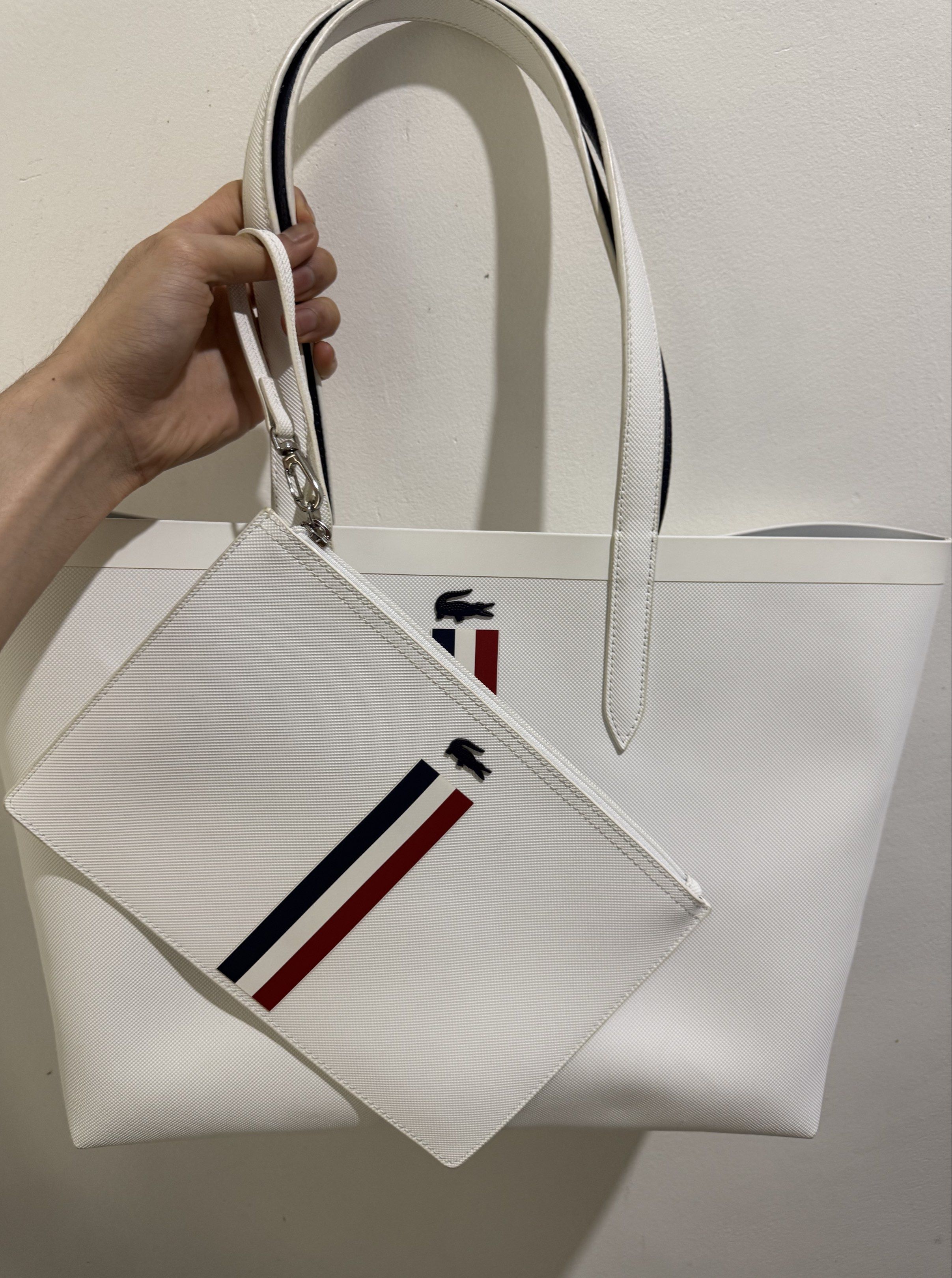 Lacoste Reversible womens large tote bag (Category: Luxury Bags & Wallets) located in Apalit. Submitted by xoxo.serena (Listing ID 1420009421, Image 1). Description: Brand: Lacoste • Color: White with classic tricolor stripe (navy/red) • Includes: Tote bag + original matching pouch • Material: Textured synthetic/leather-look material • Condition: Very good condition (no visible stains or damage) • Spacious interior, perfect for daily use, school,