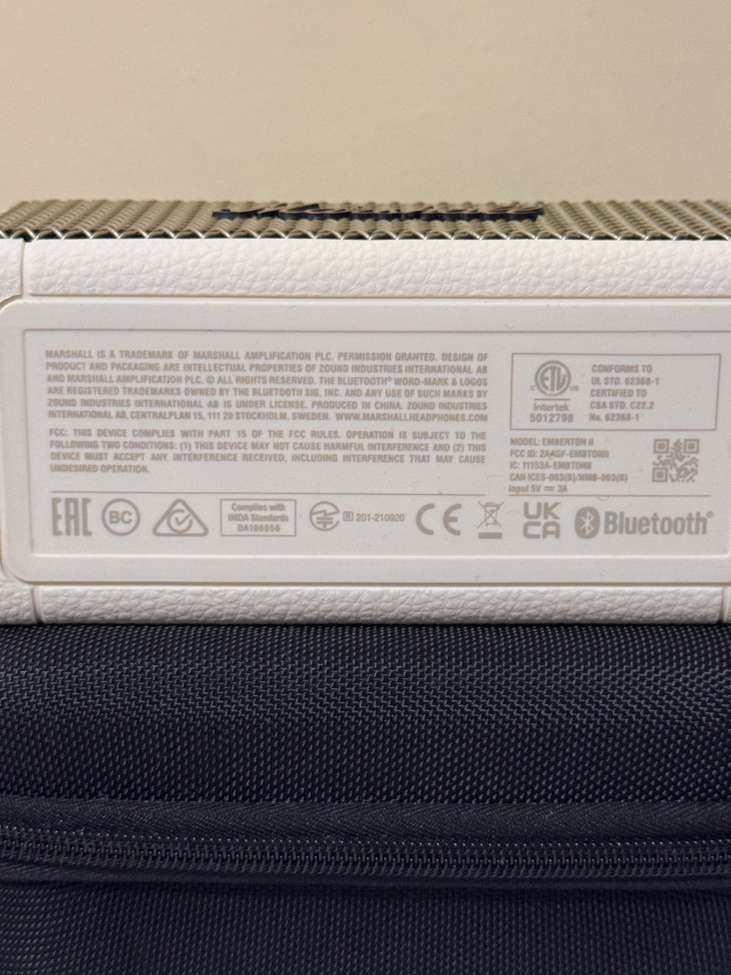 Marshall Emberton II Portable Bluetooth Speaker (Category: Soundbars, Speakers & Amplifiers) located in Manila. Submitted by ydnar.ph (Listing ID 1420085162, Image 3). Description: Marshall Emberton II is a compact portable Bluetooth speaker. It features a white exterior with the Marshall logo on the front. The speaker is shown with a black carrying case. The back of the speaker has a power input. The bottom of the speaker has the model informati