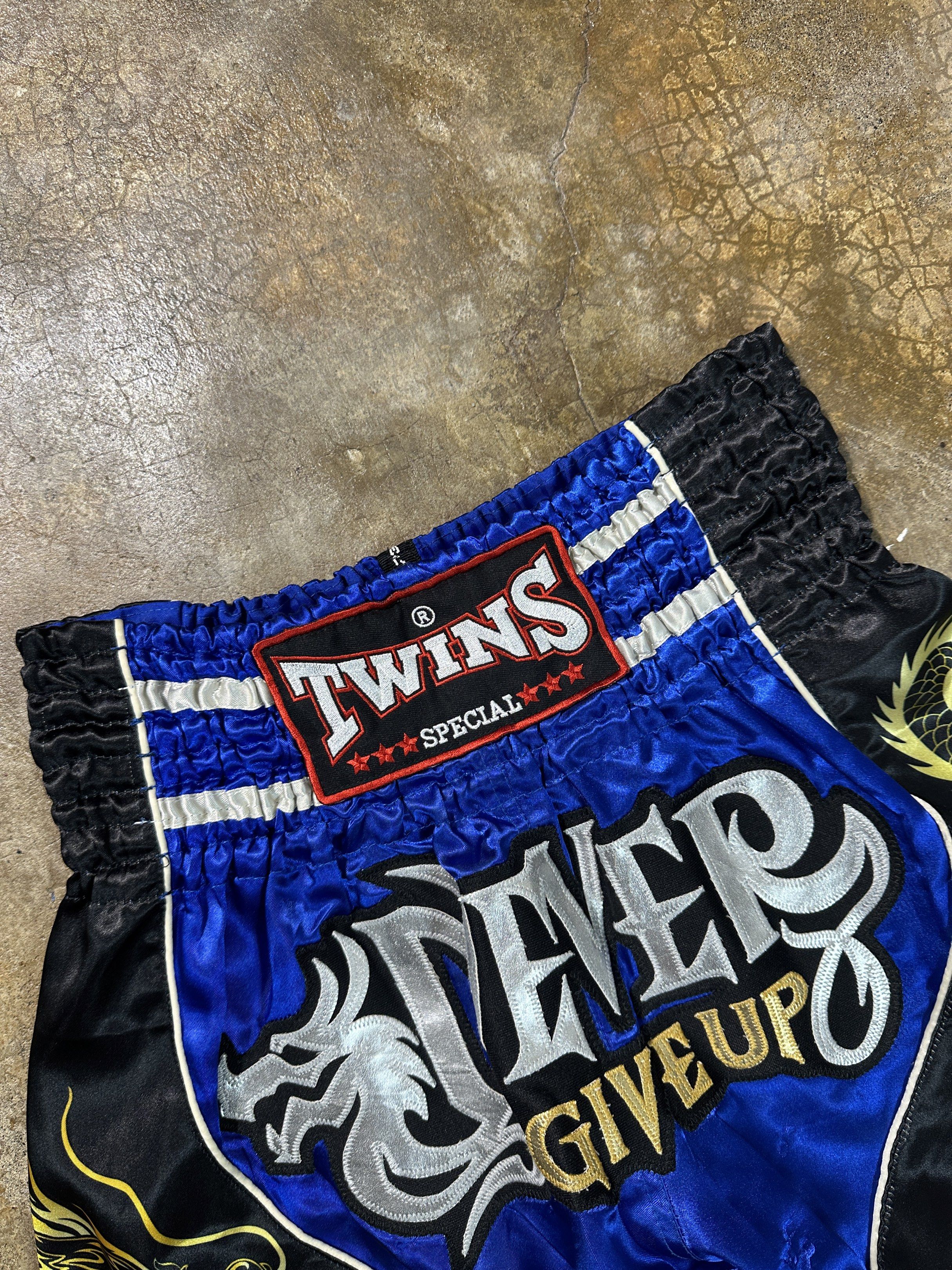 Twins Special Muay Thai Shorts - Blue (Category: Activewear) located in Bacolod City. Submitted by thestitchph (Listing ID 1420000342, Image 2). Description: - Authentic Twins Special Muay Thai shorts - Vibrant blue and black design - Features dragon graphics - "Never Give Up" slogan - Twins Special logo on waistband - Size L.