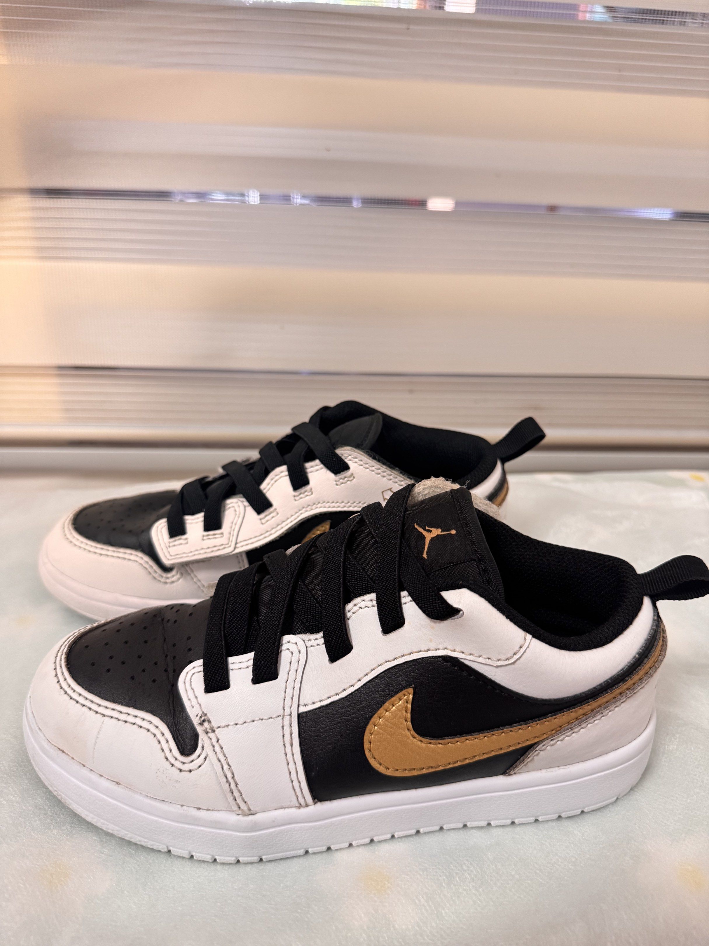 Nike Jordan 1 Low Black White Gold (Category: Sneakers) located in Silay City. Submitted by declutterwithm3 (Listing ID 1420340896, Image 2). Description: - Nike Jordan 1 Low Kids sneakers - Colorway: Black, White, Gold - Size: US 2Y / 21 cm - Low-top style - White sole - Black laces - Nike swoosh on sides - Features a pull tab for easy wear.