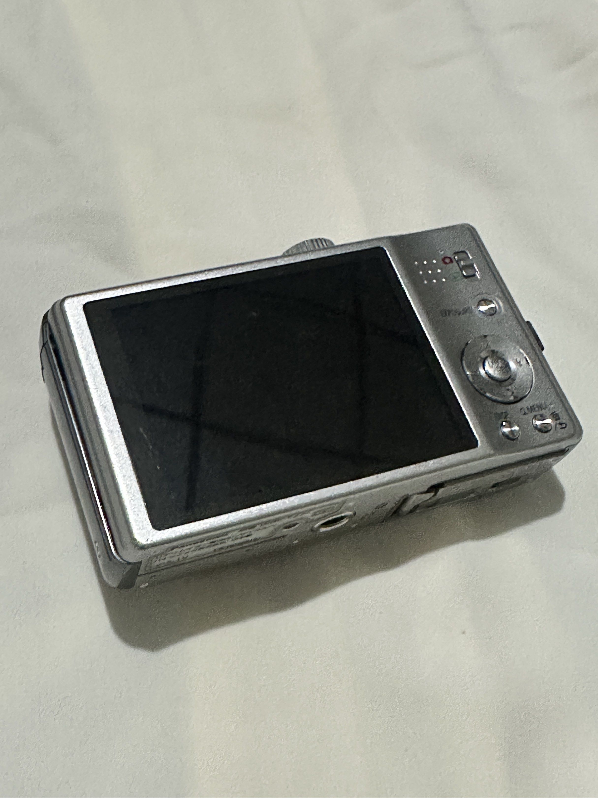 Panasonic Lumix DMC-TZ20 Digital Camera (Category: Cameras) located in Manila. Submitted by naaadaaaa (Listing ID 1420273535, Image 2). Description: Panasonic Lumix DMC-TZ20 digital camera with Leica lens. Features 16x zoom and full HD video recording. Includes GPS. The camera shows a system error related to focus. Battery and memory card slot are visible. The camera is silver in color. Zoom quality in pictures and vids are very nice!!! (Can send