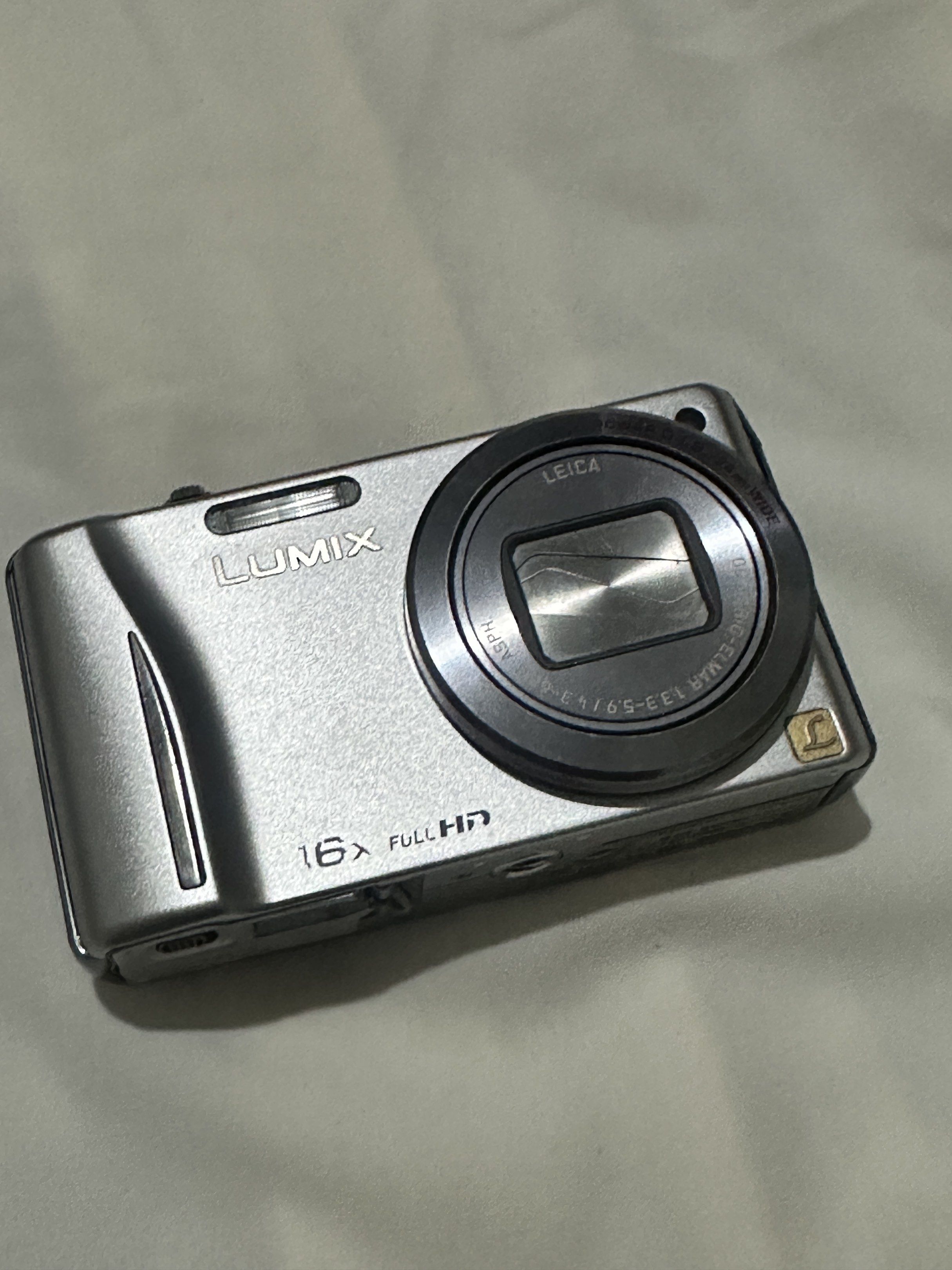 Panasonic Lumix DMC-TZ20 Digital Camera (Category: Cameras) located in Manila. Submitted by naaadaaaa (Listing ID 1420273535, Image 1). Description: Panasonic Lumix DMC-TZ20 digital camera with Leica lens. Features 16x zoom and full HD video recording. Includes GPS. The camera shows a system error related to focus. Battery and memory card slot are visible. The camera is silver in color. Zoom quality in pictures and vids are very nice!!! (Can send