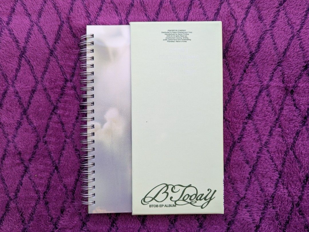 BTOB - B Today EP Album (Category: CDs & DVDs) located in Tandag. Submitted by mooncrate (Listing ID 1420356200, Image 1). Description: - BTOB's 'B Today' EP Album - Features a white album cover with a stylized title. - Unique spiral binding. - Includes text at the top of the cover. - Set against a purple fabric background..