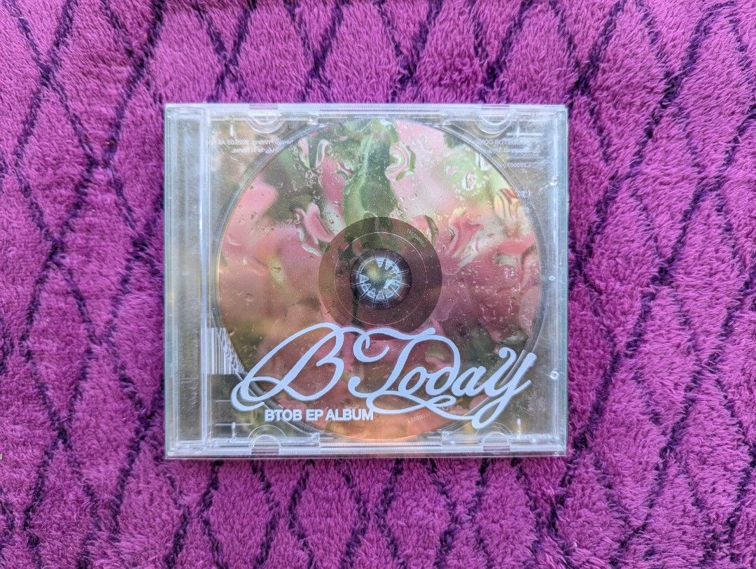 BTOB - B Today EP Album (Category: CDs & DVDs) located in Tandag. Submitted by mooncrate (Listing ID 1420356200, Image 2). Description: - BTOB's 'B Today' EP Album - Features a white album cover with a stylized title. - Unique spiral binding. - Includes text at the top of the cover. - Set against a purple fabric background..