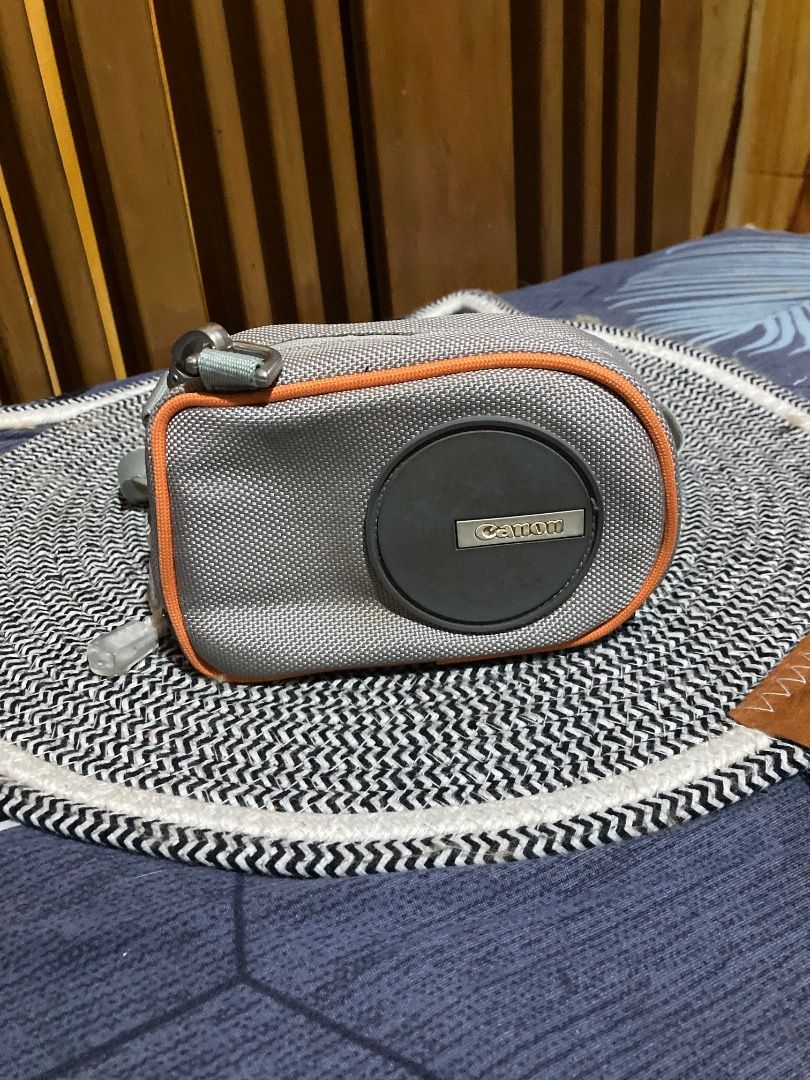 Canon Camera Bag with Strap (Category: Camera Bags & Carriers) located in La Trinidad. Submitted by clawver123 (Listing ID 1420489815, Image 1). Description: - Canon camera bag for protection - Gray exterior with orange trim - Features the Canon logo - Detachable shoulder strap included - Black fabric interior - Secure zippered closure.
