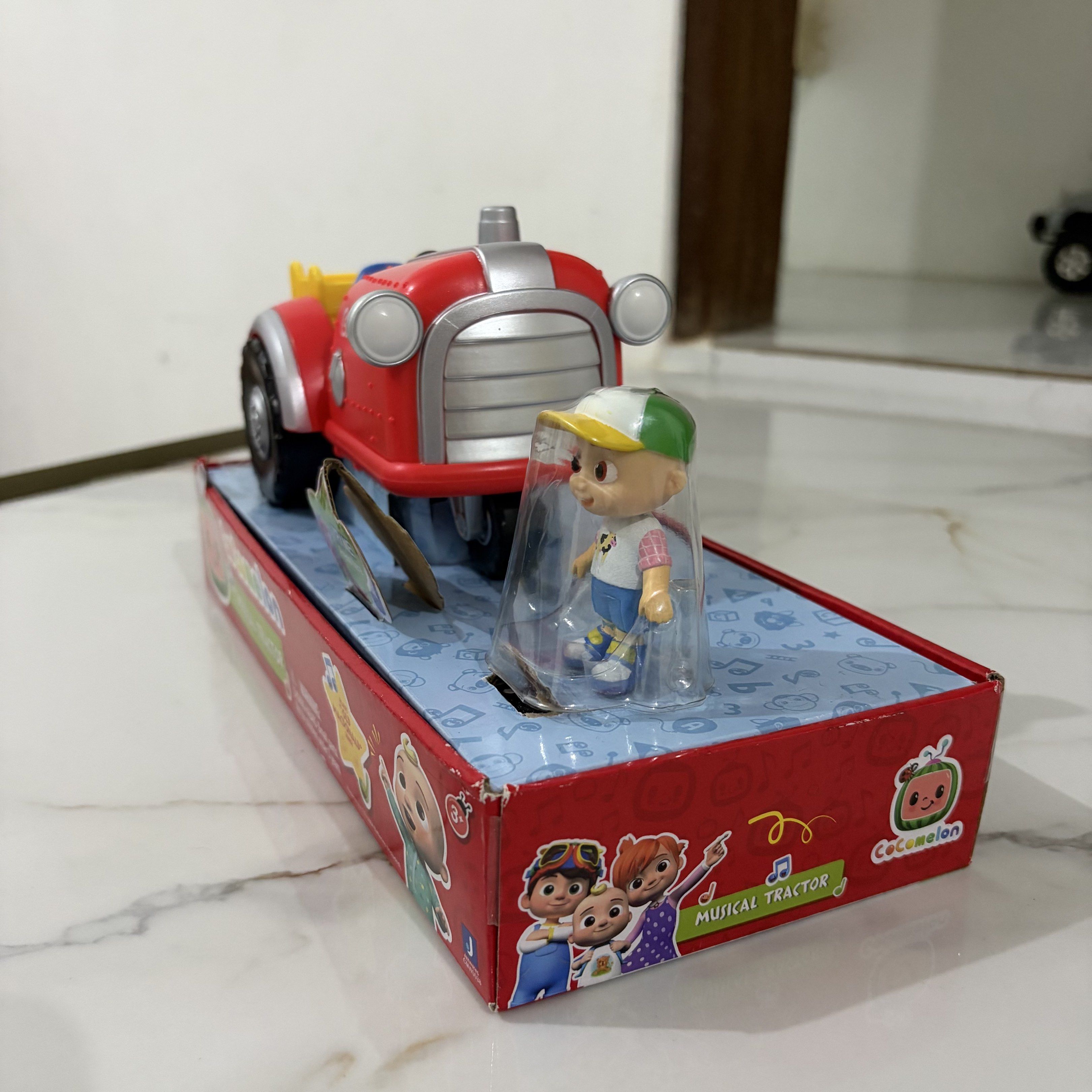 CoComelon Musical Tractor Toy (Category: Kids Toys) located in Bulacan. Submitted by speczone (Listing ID 1420497446, Image 3). Description: - CoComelon Musical Tractor toy included. - Comes with a figure. - Tractor color: Red with black wheels and yellow bed. - Features the 'Try Me! Press here' button. - Box features the CoComelon logo and 'Musical Tractor' text. - from US box (padala from a relative).