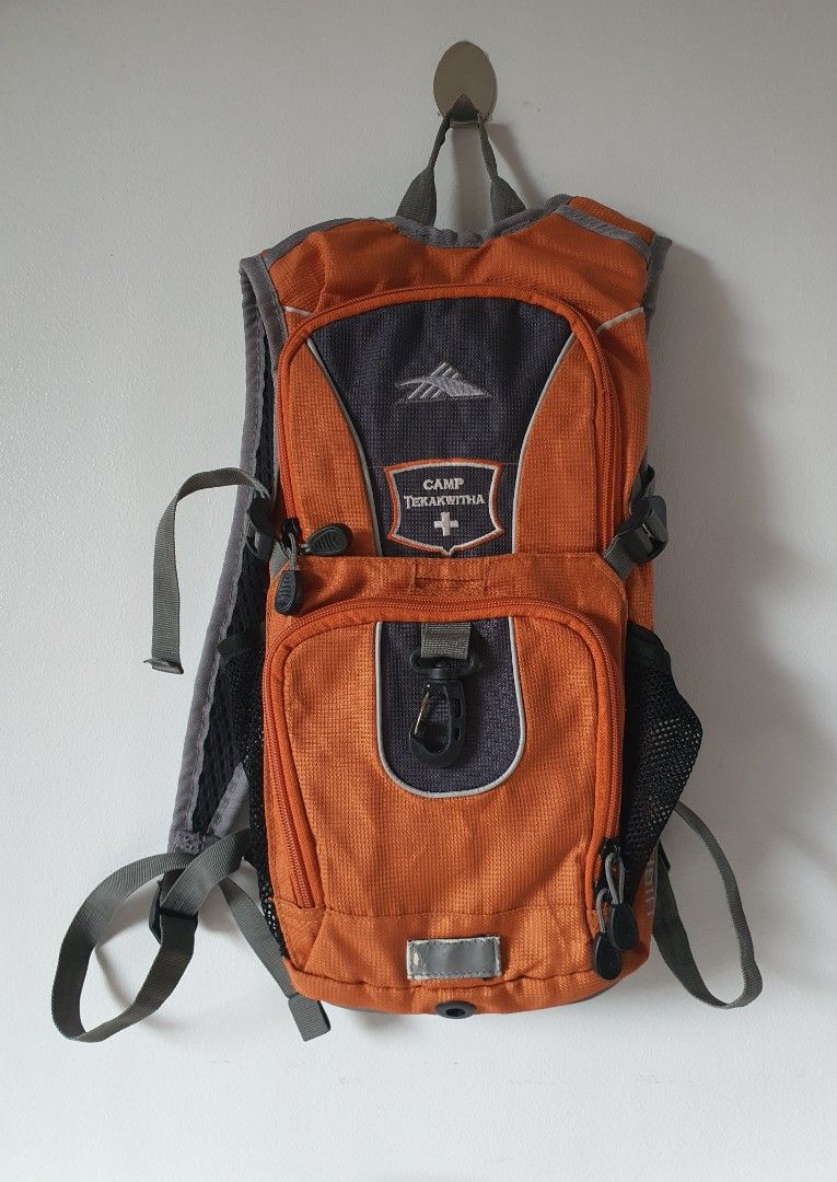 High Sierra Camp Tekakwitha Hydration Backpack (Category: Backpacks) located in Meycauayan. Submitted by shoptoown (Listing ID 1420365173, Image 1). Description: - Orange and gray hydration backpack - Features the "Camp Tekakwitha" logo - Multiple compartments for storage - Adjustable straps for a comfortable fit - Breathable mesh back panel - High Sierra branded clips and zipper pulls - Designed for outdoor activities.