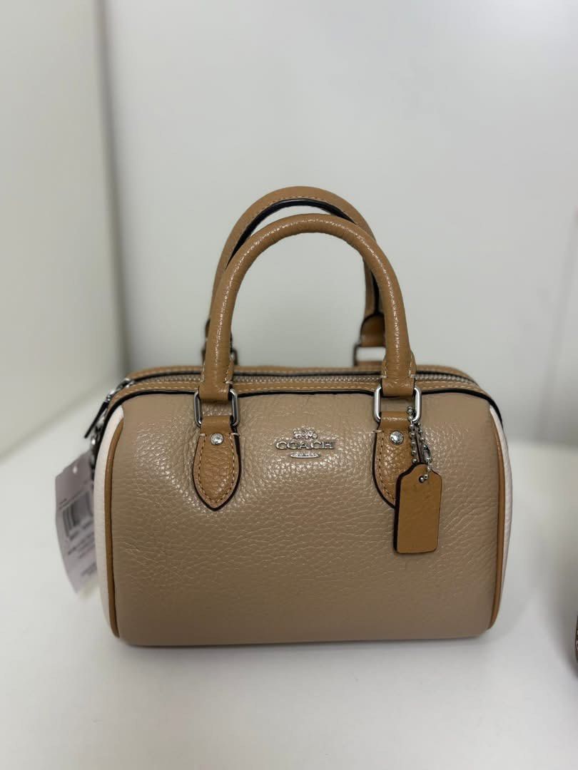 Mini Barrel Rowan Bag (Category: Luxury Bags & Wallets) located in Manila. Submitted by lovieauthenticmerchandise (Listing ID 1420492045, Image 1). Description: - Coach Mini Barrel Bag - Dual-tone design: tan body, white accents - Top handle and detachable shoulder strap - Features Coach hangtag - Zippered closure - Brown fabric interior lining - Compact size, perfect for essentials.