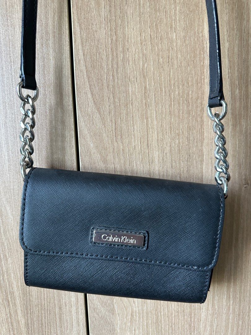 Calvin Klein Black Crossbody Bag (Category: Cross-body Bags) located in Quezon City. Submitted by sofieegee (Listing ID 1420651042, Image 2). Description: - Black Calvin Klein crossbody bag - Silver chain strap - Flap closure with magnetic snap - Interior: card slots and zippered pocket - Textured finish - Calvin Klein logo on front.