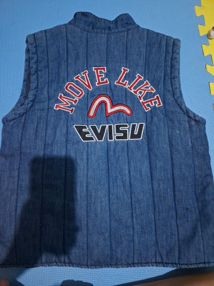 Evisu Denim Vest (Category: Vests) located in Manila. Submitted by wildcat-9fb3 (Listing ID 1420644132, Image 2). Description: - Denim vest - Mandarin collar - Toggle closures - Two front pockets - Small logo - Embroidered "MOVE LIKE EVISU" on the back (red and white) - Quilted - Denim material Never used. Send chat for more pictures. buyer will shoulder the delivery fee :).