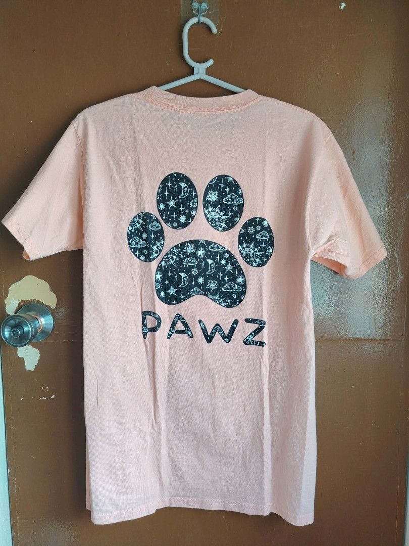 PAWZ Graphic T-Shirt (Category: Tshirts & Polo Shirts ) located in Pasay City. Submitted by ceeeeee (Listing ID 1420621631, Image 2). Description: - Peach-colored t-shirt - Paw print design - Space-themed pattern on the back - Small paw print logo on the front - "PAWZ" printed below the logo - Short sleeves - Crew neck.