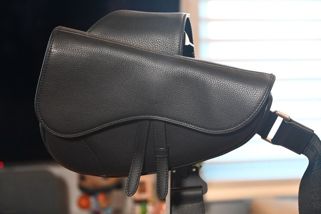 Christian Dior Saddle Bag Black - Men's (Category: Luxury Bags & Wallets) located in Muntinlupa City. Submitted by honestlygood (Listing ID 1423982570, Image 1). Description: Black leather saddle bag from Christian Dior. Features an adjustable strap with a metal buckle closure. The bag has a curved shape with a flap closure. The strap has the Christian Dior logo..