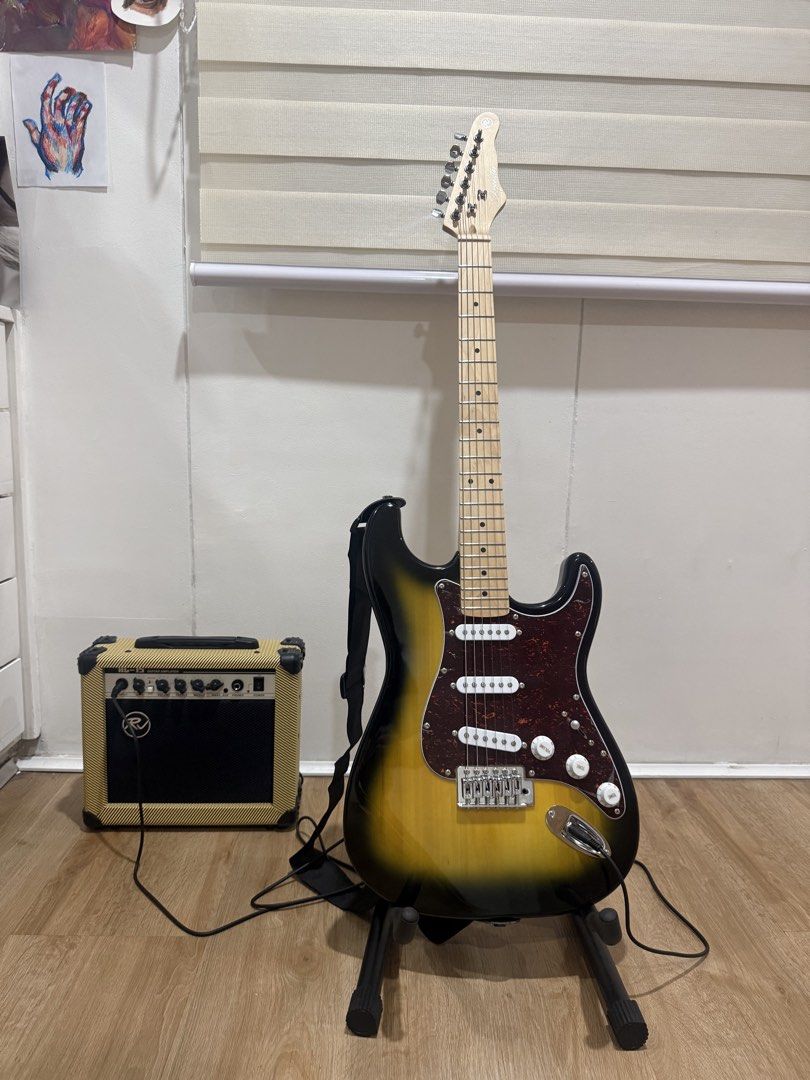 Electric Guitar with Amplifier and Accessories (Stratocaster) (Category: Musical Instruments) located in Manila. Submitted by archivesbyelle (Listing ID 1424152286, Image 1). Description: - Electric guitar with sunburst finish, maple fretboard, and tortoise pick guard (still has plastic on it) - RJ guitar amplifier (15 watts) - Inclusions: 2 guitar picks, strap, cable, tremolo arm, and allen wrench/keys, capo, Rixton guitar stand, Rixton guitar t