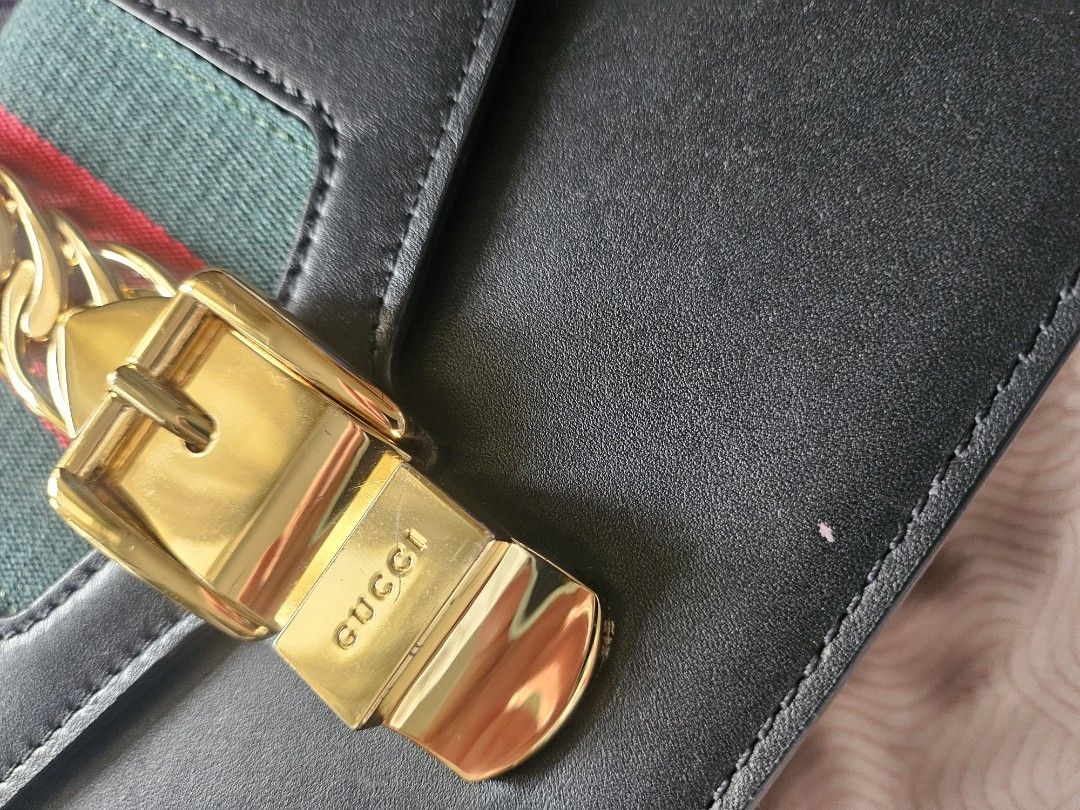 Gucci Sylvie Leather Shoulder Bag (Category: Luxury Bags & Wallets) located in Manila. Submitted by arlenitian76248 (Listing ID 1424098346, Image 2). Description: - Authentic Gucci Sylvie shoulder bag - Black leather - Gold-tone chain and buckle closure - Signature green and red stripe detail - Detachable shoulder strap with red, navy, and green stripes - Interior slip pocket - Includes Gucci La Tigre card.