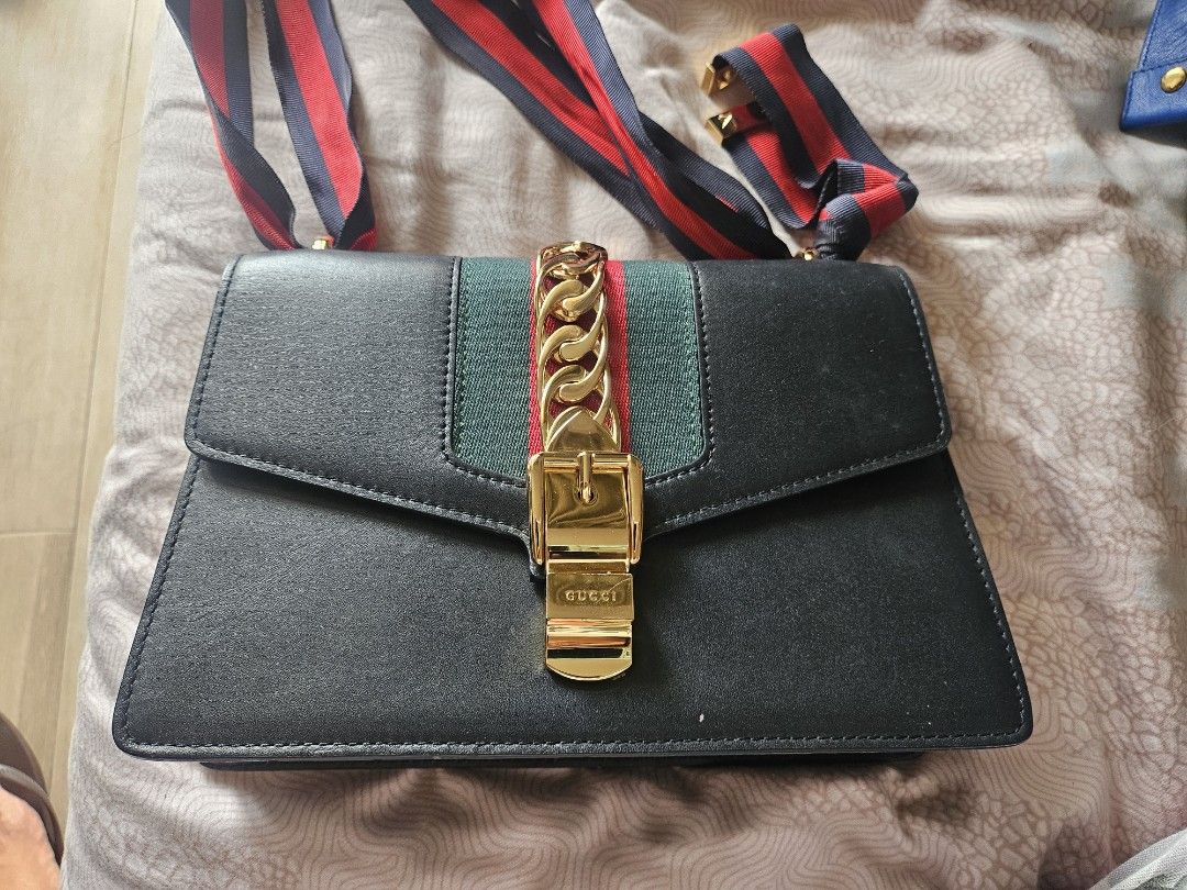 Gucci Sylvie Leather Shoulder Bag (Category: Luxury Bags & Wallets) located in Manila. Submitted by arlenitian76248 (Listing ID 1424098346, Image 1). Description: - Authentic Gucci Sylvie shoulder bag - Black leather - Gold-tone chain and buckle closure - Signature green and red stripe detail - Detachable shoulder strap with red, navy, and green stripes - Interior slip pocket - Includes Gucci La Tigre card.
