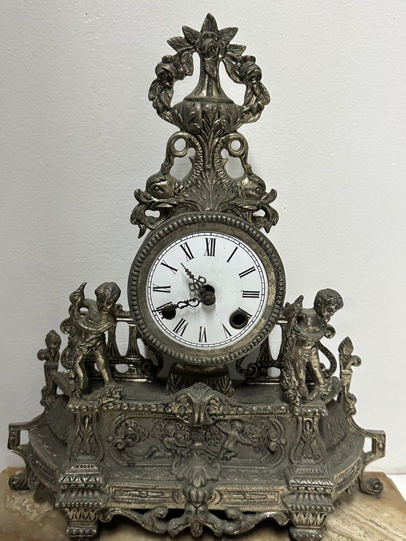 Vintage Decorative Clock (Category: Clocks) located in Quezon City. Submitted by anjherga27 (Listing ID 1423994230, Image 2). Description: - Antique clock - Roman numeral display - Decorative cherub figures - Ornate metal detailing - Elegant marble base - Visible clock mechanism.