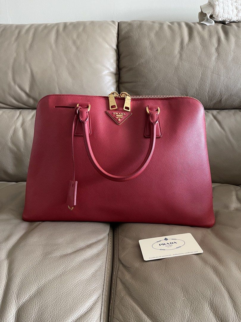 Prada Saffiano Leather Tote Bag Alma (Category: Luxury Bags & Wallets) located in Makati City. Submitted by markussangabriel (Listing ID 1425732285, Image 1). Description: Authentic Prada tote bag in a vibrant red color. Features gold-tone hardware, including zippers and the Prada logo. The bag has a top zipper closure and dual top handles. Includes an interior with multiple compartments and a Prada authenticity card..