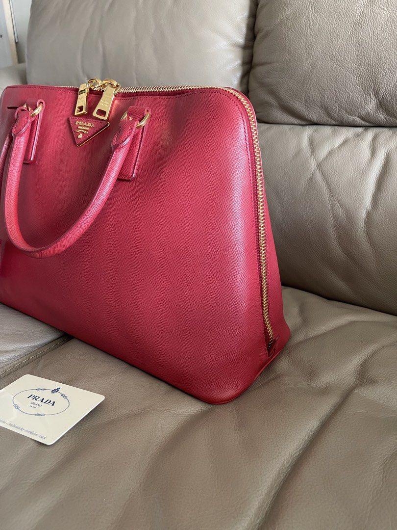Prada Saffiano Leather Tote Bag Alma (Category: Luxury Bags & Wallets) located in Makati City. Submitted by markussangabriel (Listing ID 1425732285, Image 2). Description: Authentic Prada tote bag in a vibrant red color. Features gold-tone hardware, including zippers and the Prada logo. The bag has a top zipper closure and dual top handles. Includes an interior with multiple compartments and a Prada authenticity card..