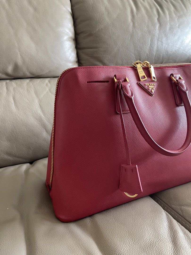 Prada Saffiano Leather Tote Bag Alma (Category: Luxury Bags & Wallets) located in Makati City. Submitted by markussangabriel (Listing ID 1425732285, Image 3). Description: Authentic Prada tote bag in a vibrant red color. Features gold-tone hardware, including zippers and the Prada logo. The bag has a top zipper closure and dual top handles. Includes an interior with multiple compartments and a Prada authenticity card..