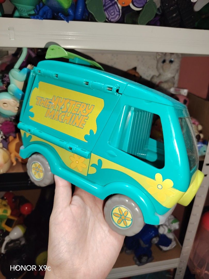Scooby Doo Mystery Machine Van Toy (Category: Vehicle & Diecast Models) located in Iligan City. Submitted by shehabdor98515 (Listing ID 1425818761, Image 3). Description: Scooby Doo Mystery Machine van toy. It features the iconic teal and yellow color scheme with flower details. The van has opening compartments. The wheels are gray with yellow flower details. The Mystery Machine logo is visible on the side of the van..