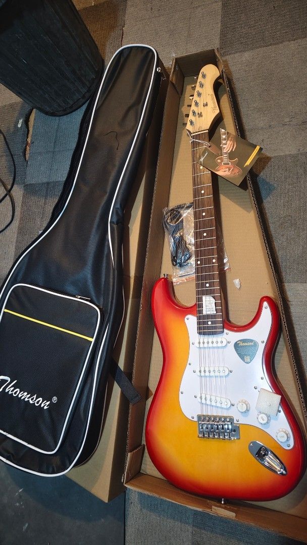 electric guitar Thomson Electric Guitar with Case (Category: Musical Instruments) located in Pasig City. Submitted by tupriomichaeljohn (Listing ID 1425881849, Image 2). Description: Thomson electric guitar with a carrying case. Available in black, sunburst, blue, and brown. Includes a guitar case, cable, and accessories. The guitar has a white pickguard and a maple neck. The headstock has the Thomson logo. Perfect for beginners or experienced pl
