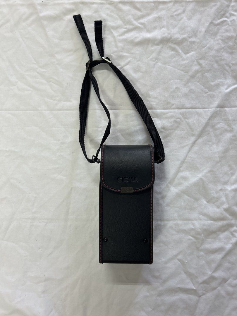 Sigma Camera Case with Strap (Category: Camera Bags & Carriers) located in Bulacan. Submitted by ourdailybreads (Listing ID 1425841402, Image 1). Description: Black Sigma camera case with a red stitched trim. Includes a black strap for carrying. The case has a rectangular shape with a flap closure. The Sigma logo is visible on the front..
