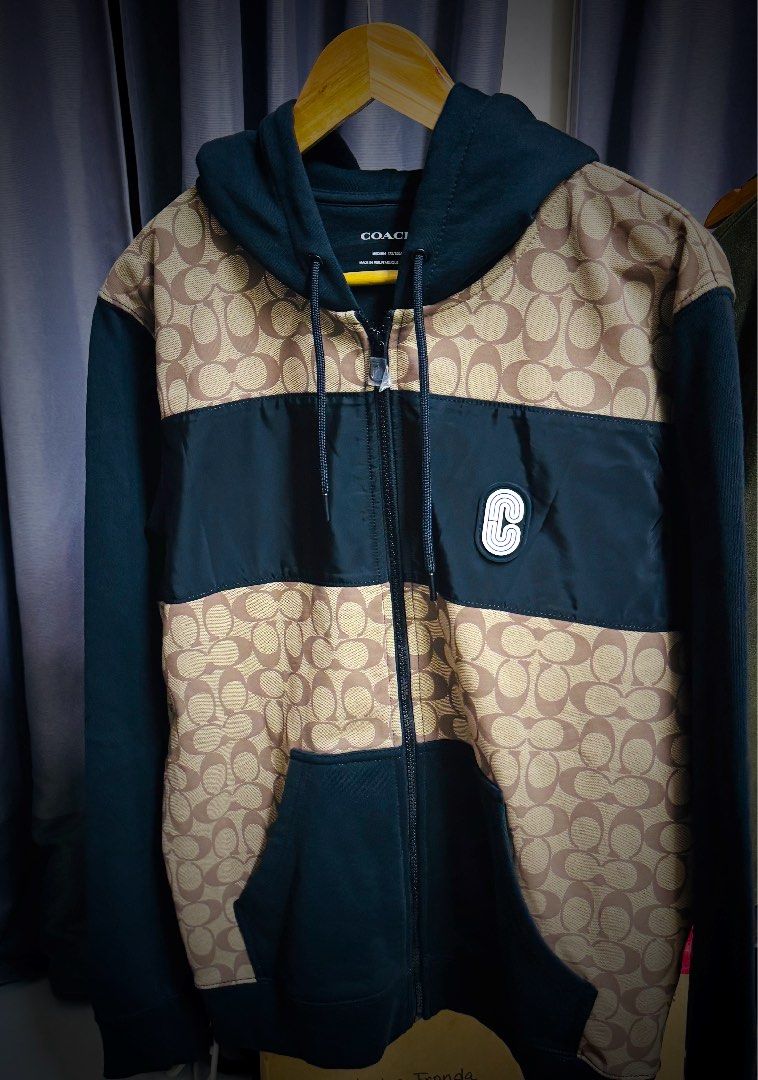 Coach Signature Hoodie - Medium (Category: Luxury Apparel) located in Batangas. Submitted by cjayf (Listing ID 1426123662, Image 2). Description: Authentic Coach hoodie featuring the signature Coach pattern. It has a black hood, sleeves, and pockets, with a zip-up front. The size is medium, as indicated on the label. Made in Peru. The hoodie has a "C" logo patch on the chest. The fabric composition is 100% cotton for the body and hood lining..
