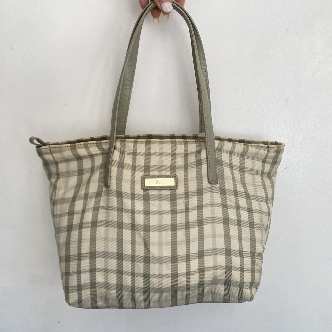 DAKS London Plaid Tote Medium Bag (Category: Tote Bags) located in Roxas City. Submitted by rglnos (Listing ID 1426020078, Image 1). Description: DAKS London tote bag features a classic plaid pattern in neutral tones. It has a top zipper closure and a spacious interior. The bag includes a small interior pocket and a magnetic snap closure. The handles and trim are a matching solid color. The bag has a metal DAKS logo on the front..