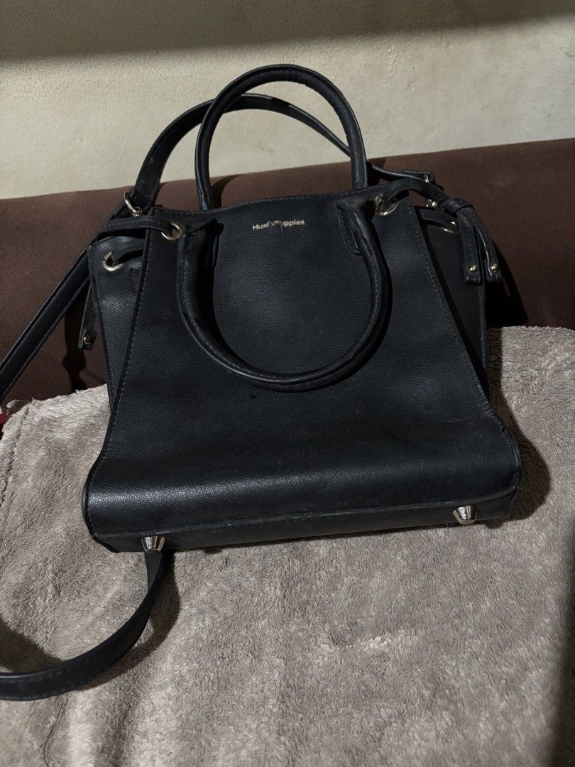 Hush Puppies Black Handbag (Category: Luxury Bags & Wallets) located in Batangas. Submitted by mylenevillegas-21 (Listing ID 1426150202, Image 3). Description: Black Hush Puppies handbag with top handles and a detachable shoulder strap. Features a magnetic snap closure and a zippered interior pocket. The bag has a structured shape with metal feet on the bottom. The interior is lined with fabric and includes a brand label. The exterior has a subtl