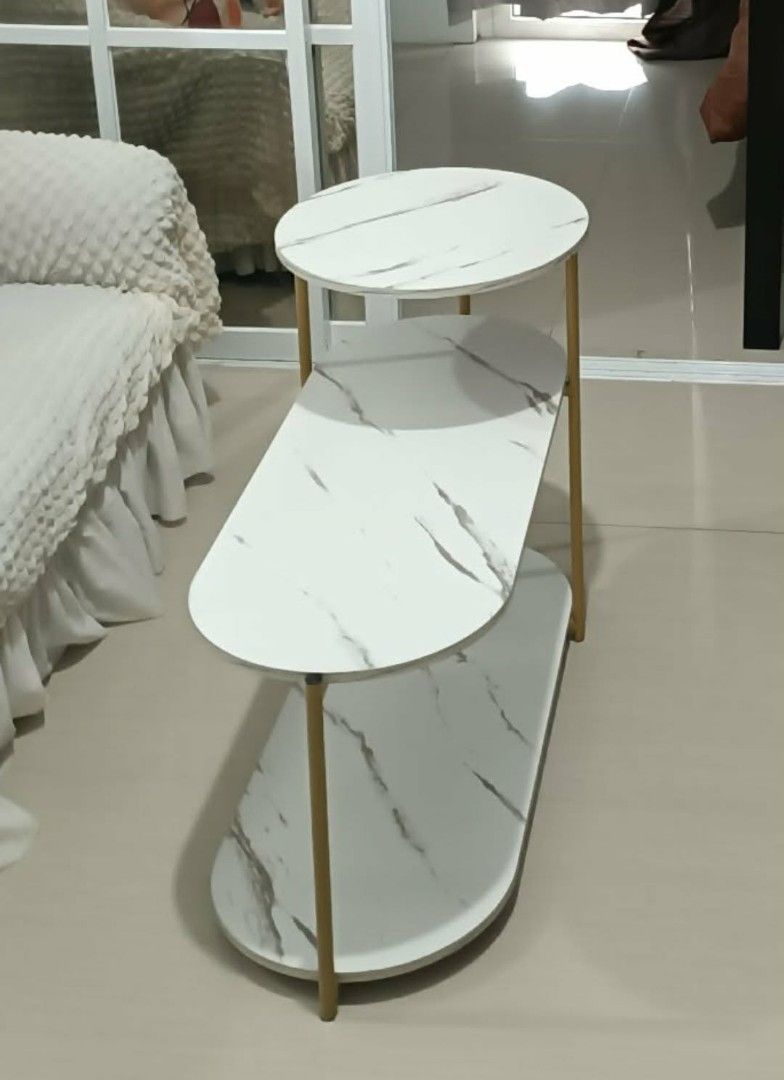 Marble Top Side Table with Gold Frame (Category: Tables & Sets) located in Caloocan City. Submitted by mommymoon71 (Listing ID 1426179295, Image 1). Description: Stylish side table featuring a white marble-look top and a gold-colored frame. It has three tiers, with a round top and two lower shelves with a unique shape. Perfect for placing beside a sofa or bed for added convenience. The table offers a modern and elegant touch to any living space..