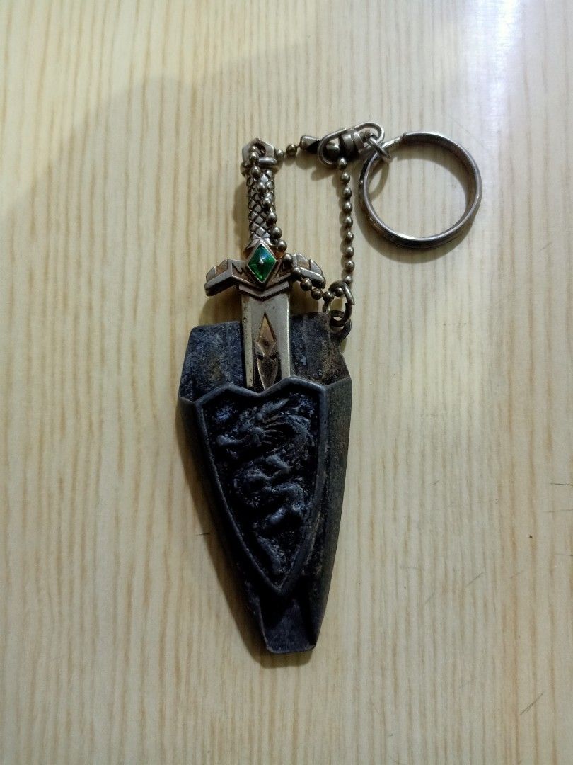 Phantom spirit Dragon Keychain (Category: Character Goods) located in Las Pinas. Submitted by the_recycle_shop (Listing ID 1426158566, Image 2). Description: Keychain features a sword and shield design with a dragon motif. The sword has a green gem on the hilt. The shield has a dragon embossed on it. The keychain is attached to a chain and a keyring. The back of the shield has the words "Dragon Sword" engraved..