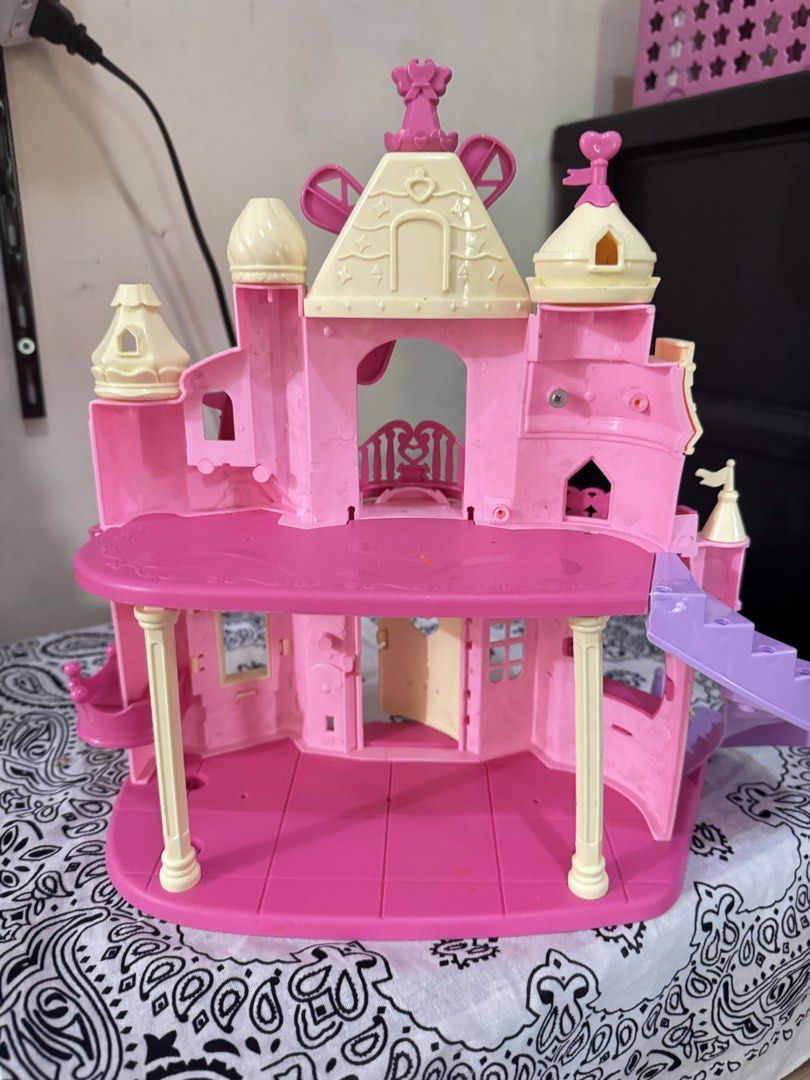 Toy Kingdom Pink Castle Playset (Category: Kids Toys) located in Paranaque City. Submitted by ledzai (Listing ID 1426033833, Image 2). Description: Pink Toy Kingdom castle playset. Size 30cmx30cm It features a windmill, stairs, and multiple rooms. The castle has a cute design with heart-shaped details. The box shows a price tag of ₱999.00. It is suitable for children aged 3 to 9yrs old. The castle is made of plastic and has a vibrant pink color.k