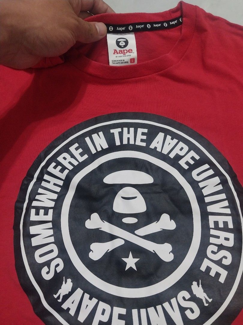 Aape by A Bathing Ape Red T-shirt (Category: Tshirts & Polo Shirts ) located in Malaybalay. Submitted by markdaumar08466 (Listing ID 1426301519, Image 2). Description: Authentic Aape by A Bathing Ape red t-shirt. Features a large graphic on the front with the text "IN THE AAPE UNIVERSE SOMEWHERE IN AAPE". The shirt has a small Aape logo on the sleeve. The tag indicates the shirt is made of 100% cotton..