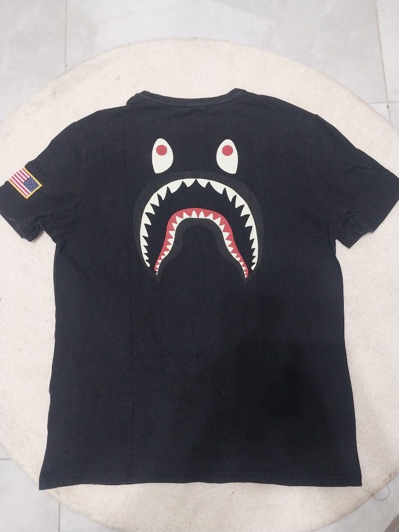 BAPE x Nike Shark Tee (Category: Tshirts & Polo Shirts ) located in Malaybalay. Submitted by markdaumar08466 (Listing ID 1426215987, Image 2). Description: Black BAPE x Nike t-shirt featuring the iconic shark design on the back and the BAPE logo on the front. It has a small Nike logo on the chest. The shirt has an American flag patch on the sleeve. It is a Dri-FIT shirt..