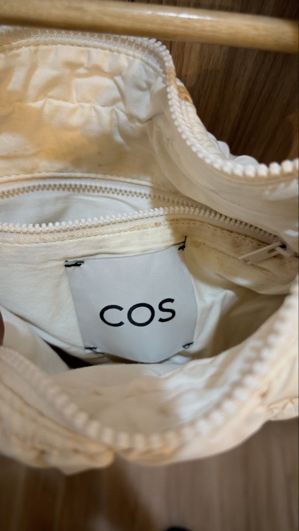 COS quilted Mini Bag (Category: Luxury Bags & Wallets) located in Alfonso. Submitted by jbcamet (Listing ID 1426297331, Image 3). Description: Cream-colored mini bag from COS. Features a quilted design and a top handle. The bag has a zipper closure. The interior has a COS label. The bag is hanging on a wooden hanger..